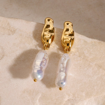 Gold waterproof earrings with pearl drops on a beige stone surface