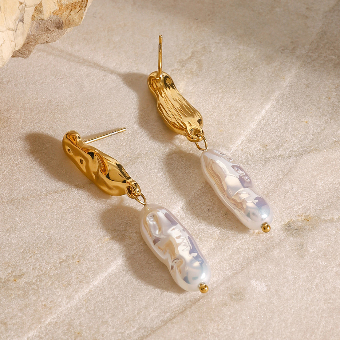 Gold earrings with pearl-like beads on a beige stone surface
