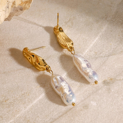 Gold earrings with pearl-like beads on a beige stone surface