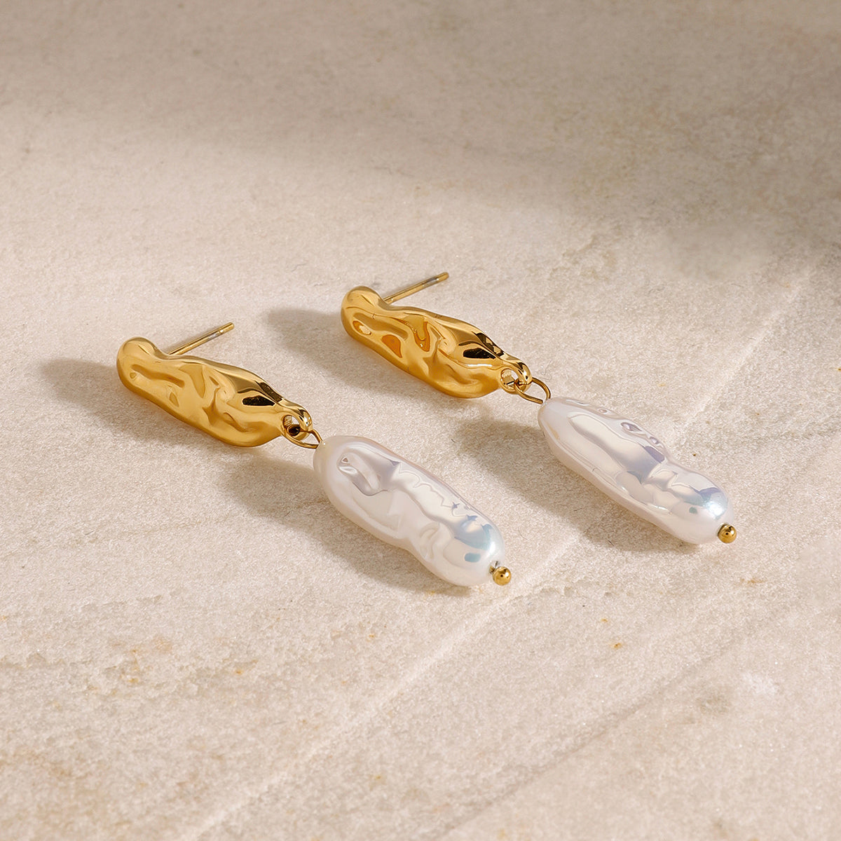 Long gold earrings with white pearl-like drops on a beige surface