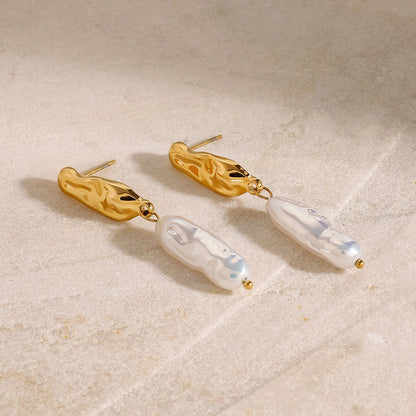 Long gold earrings with white pearl-like drops on a beige surface