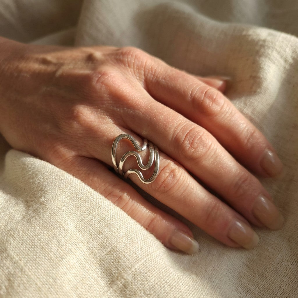 Elegant silver ring on a person's finger with a beige fabric background