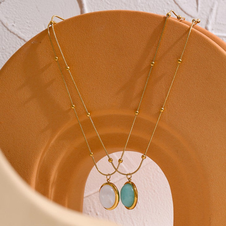 Two gold necklaces with pendant stones on a textured brown surface