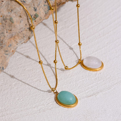 Gold necklaces with gemstone pendants on a textured white surface