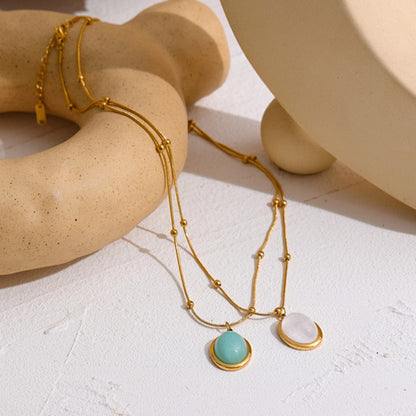 Gold necklace with turquoise and white pendants on a textured surface