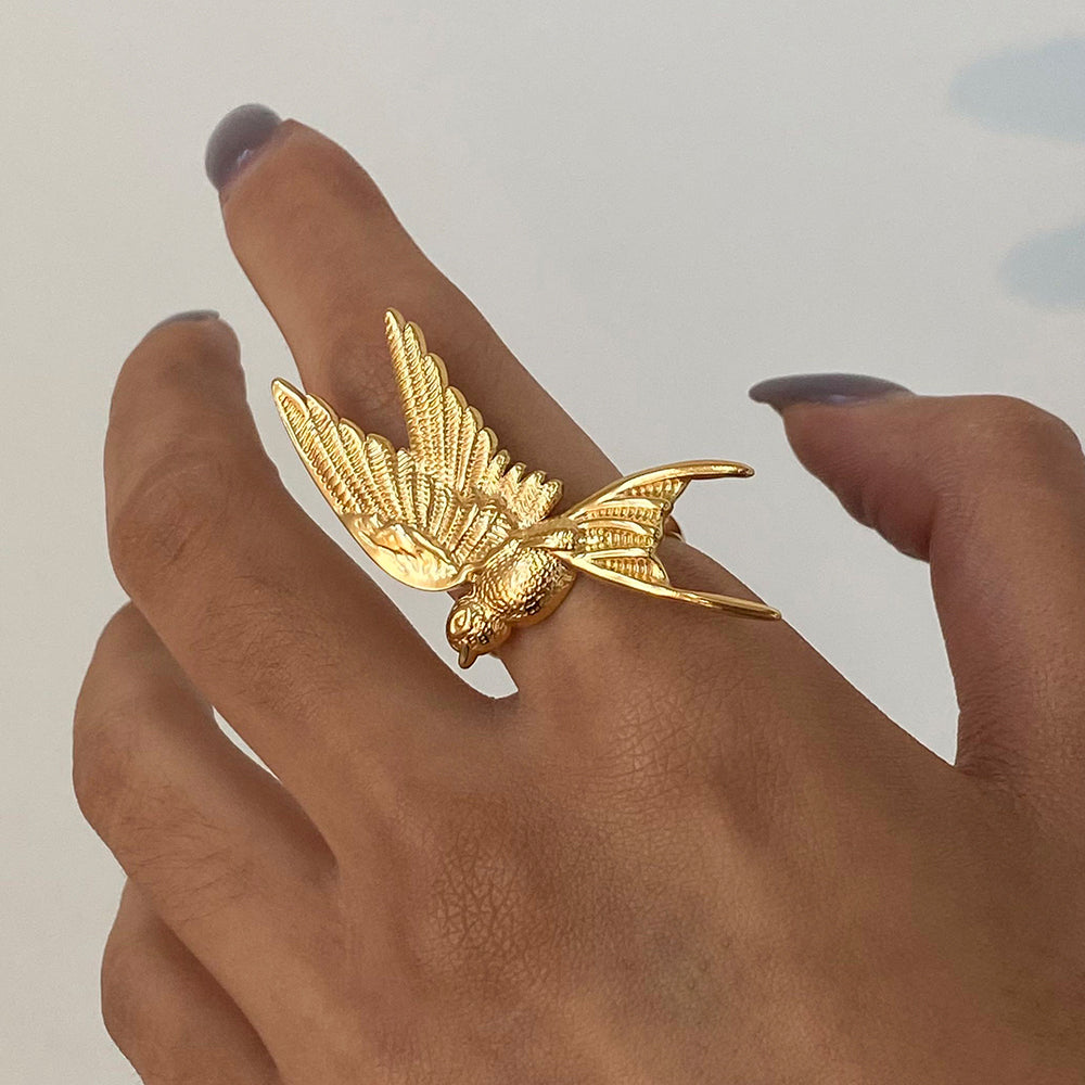 Gold bird-shaped ring on a hand with a neutral background