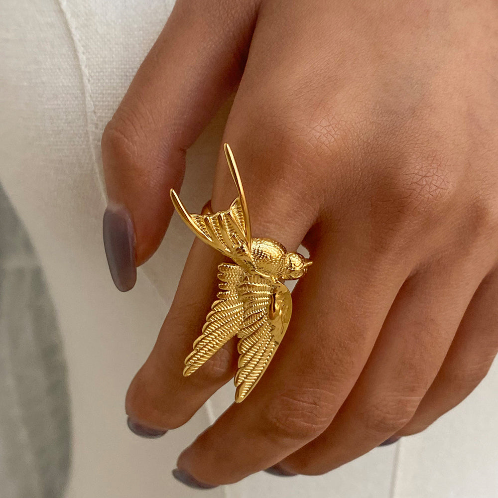 Gold bird-shaped ring on a hand with a neutral background