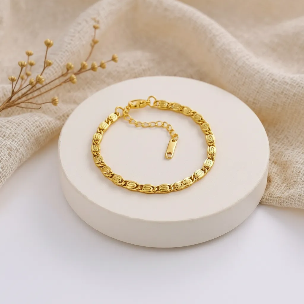 Gold bracelet on a white stone surface with beige fabric and dried flowers in the background