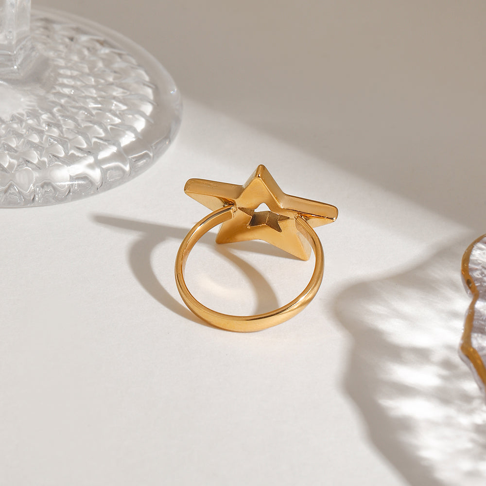 Gold star-shaped ring on a light surface with a glass object in the background