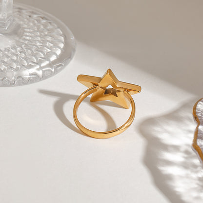 Gold star-shaped ring on a light surface with a glass object in the background