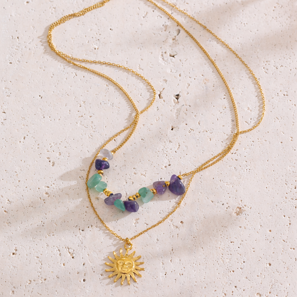 Gold necklace with sun pendant and colorful beads on a textured beige surface