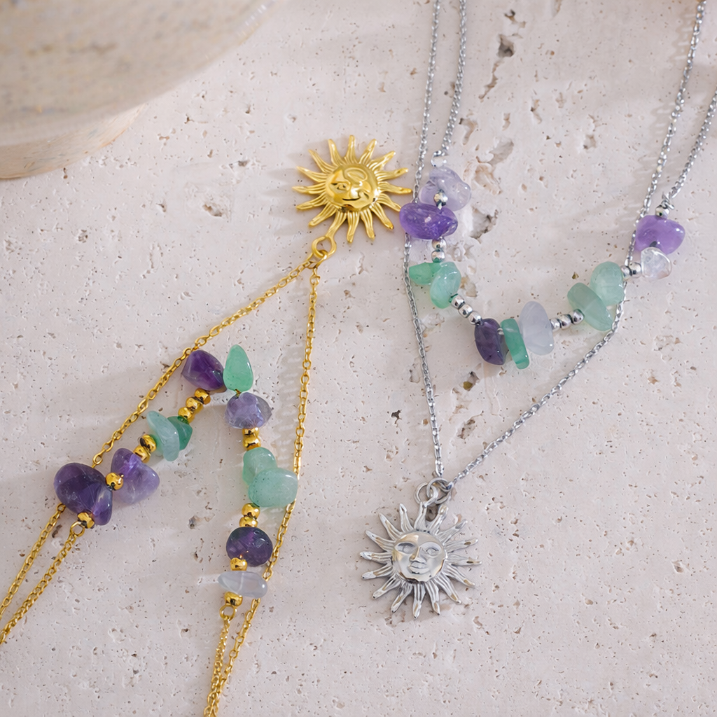 Two sun-shaped necklaces with gemstones on a textured surface