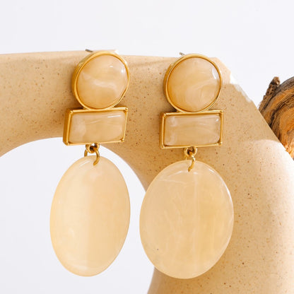 Beige earrings with gold accents on a beige stand against a white background