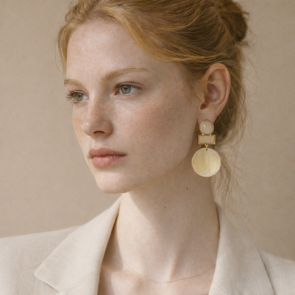 Woman wearing gold statement earrings against a beige background