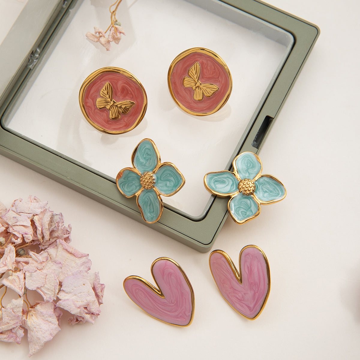Set of floral and abstract earrings on a white surface with a jewelry box in the background.