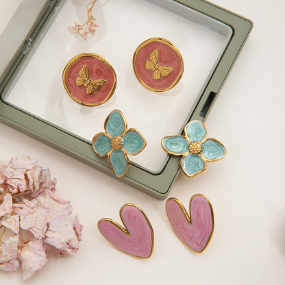 Set of floral and abstract earrings on a white surface with a jewelry box in the background.