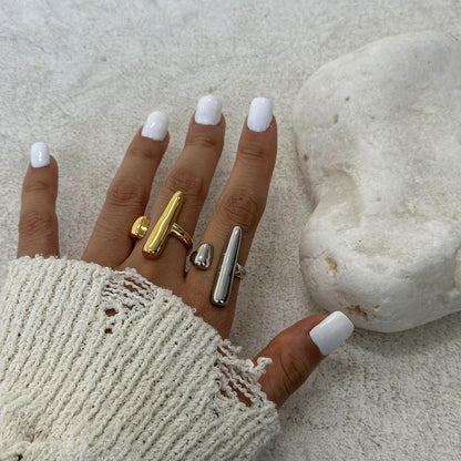 Hand wearing gold and silver rings with white nail polish against a textured surface