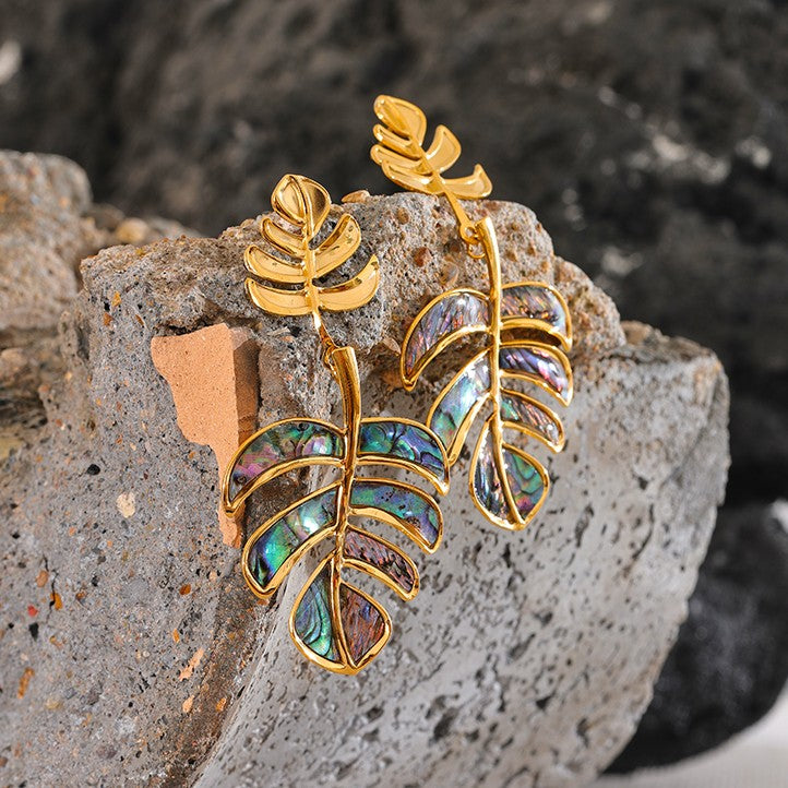 Gold leaf earrings with multicolored stones on a textured stone surface