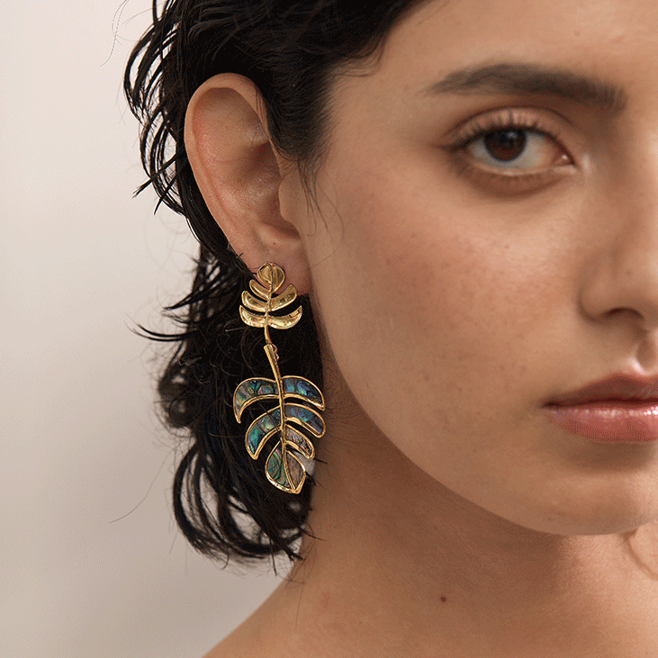 Close-up of a woman wearing a gold statement earring with a leaf design.
