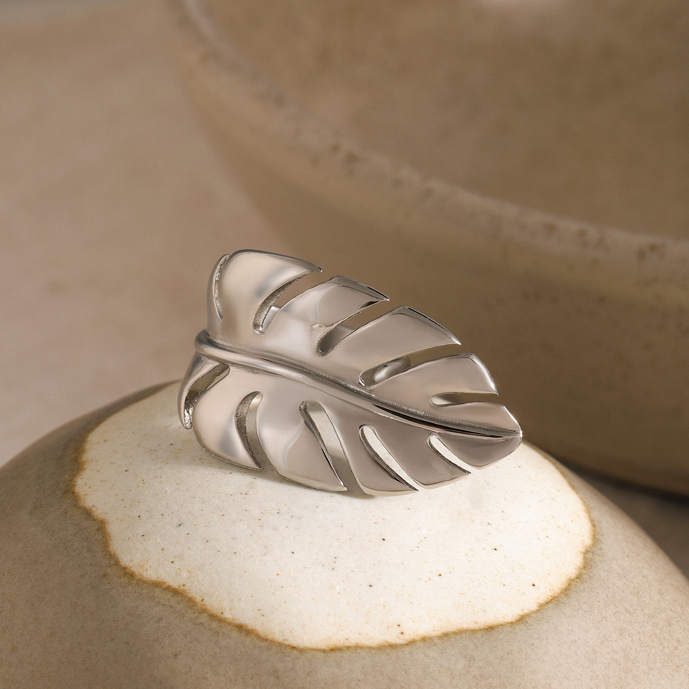 Silver leaf-shaped ring on a textured beige surface