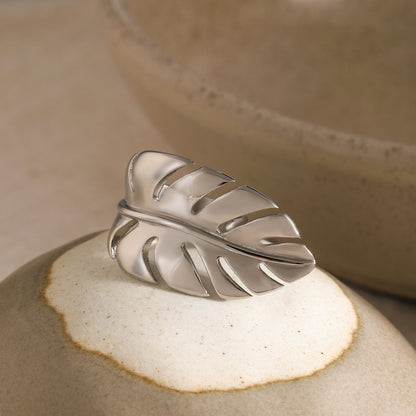 Silver leaf-shaped ring on a textured beige surface