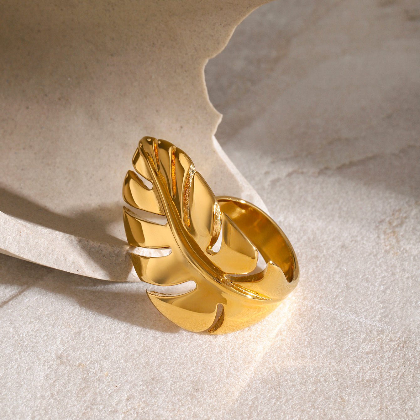 Gold chunky ring with leaf design on a textured beige background