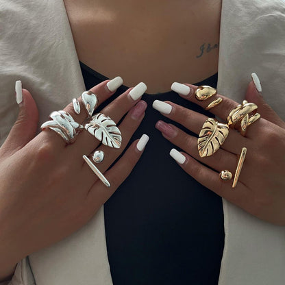 Two hands wearing various chunky rings on fingers with a neutral background