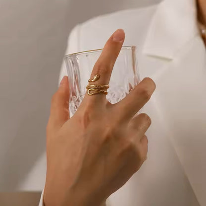 Hand wearing a gold ring holding a clear glass against a neutral background