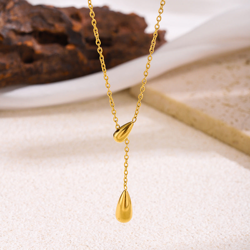 Gold necklace with teardrop pendants on a textured surface
