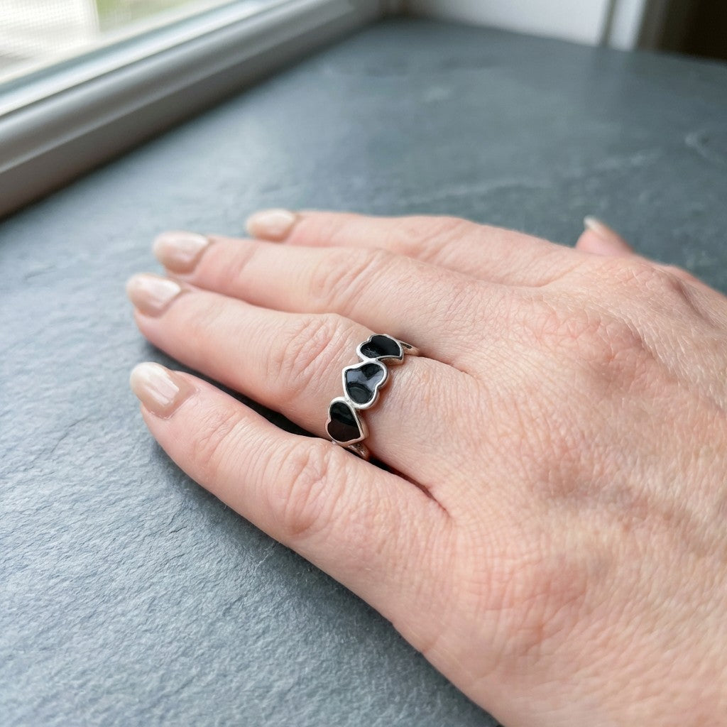 Hand wearing a tarnish-free ring with heart-shaped stones on a gray surface
