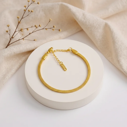 Gold bracelet on a white stand with beige fabric and dried branches in the background