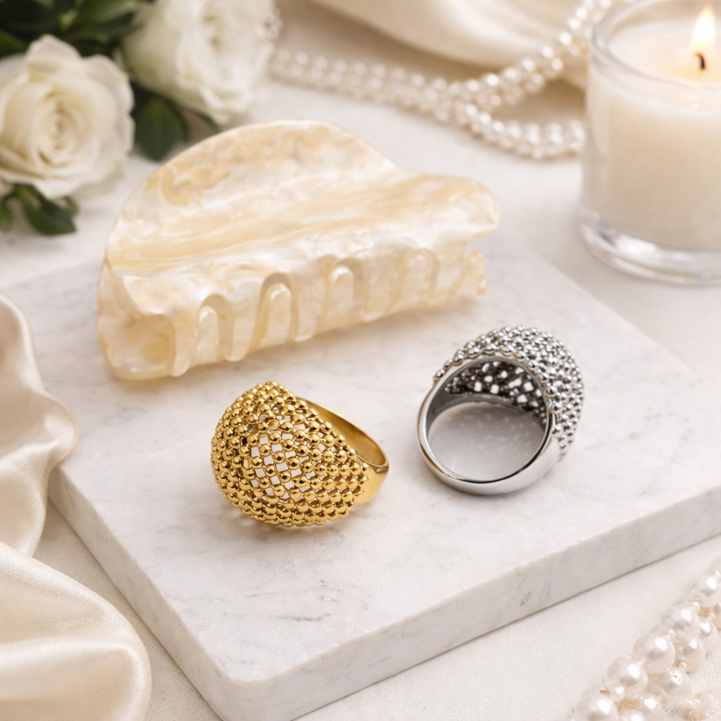 Two stainless steel rings on a marble surface with a candle and flowers in the background.