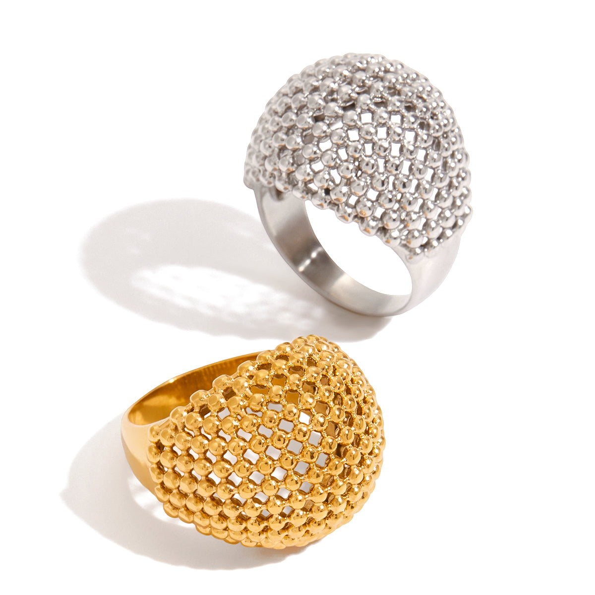 Two statement rings, one gold and one silver, on a white background