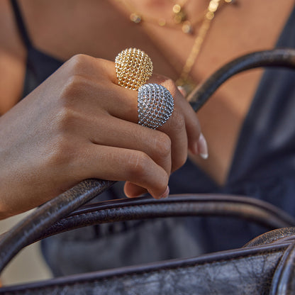 Close-up of a hand holding a brown leather handbag with two tarnish-free rings on a blurred background