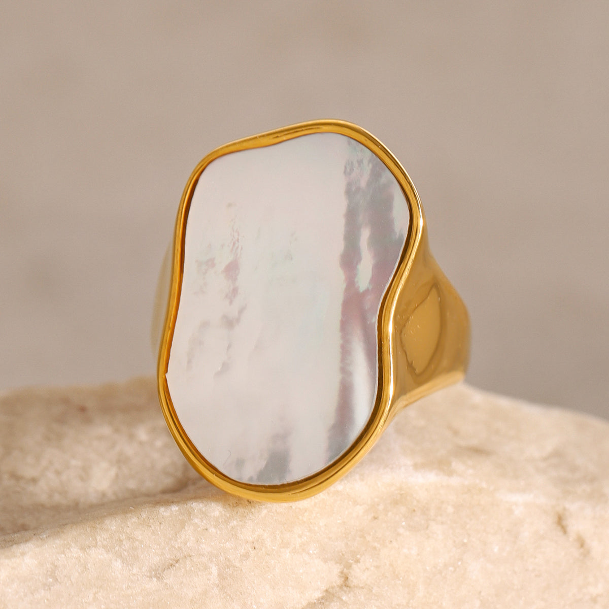 Gold ring with a large, smooth stone on a beige background