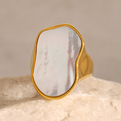 Gold ring with a large, smooth stone on a beige background