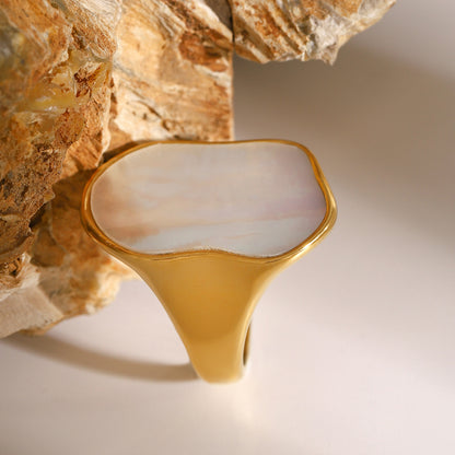 Gold ring with a white stone on a textured beige background