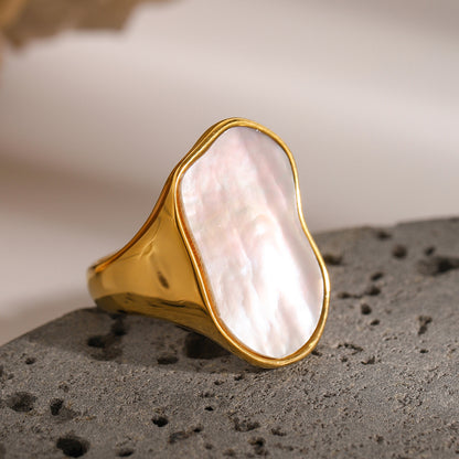 Gold ring with a large, irregularly shaped pink stone on a textured surface.