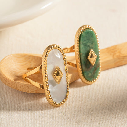 Two gold rings with green and white stones on a beige surface