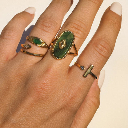 Hand wearing multiple rings with green gemstones on a neutral background