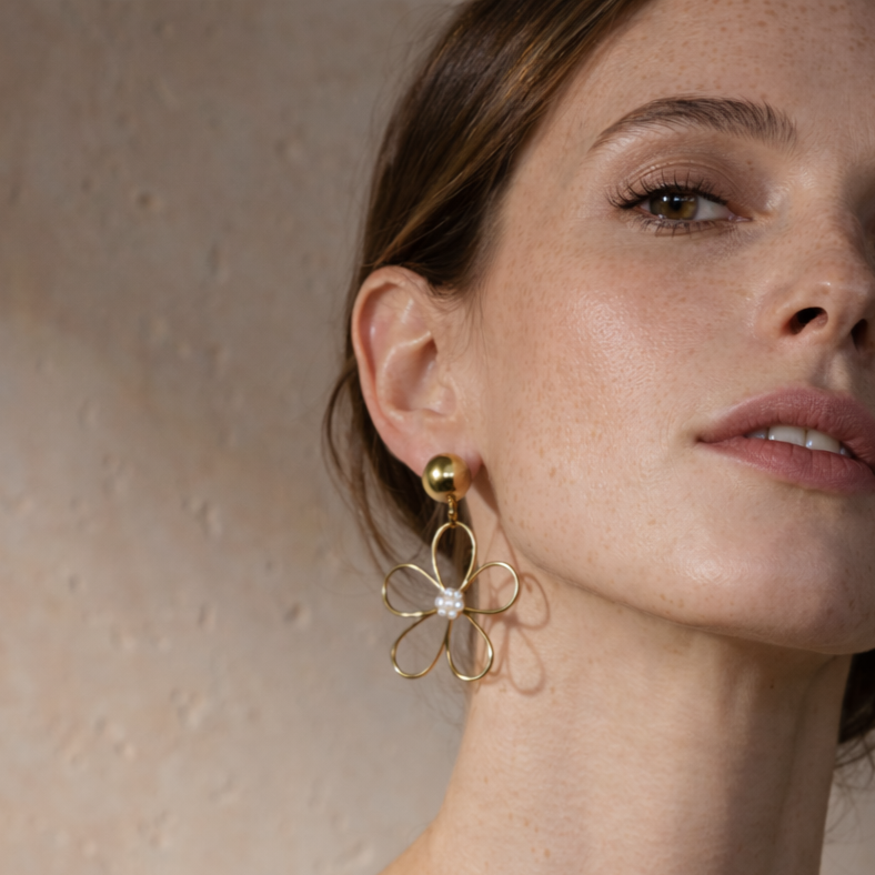 Close-up of a woman wearing gold flower-shaped earrings against a neutral background