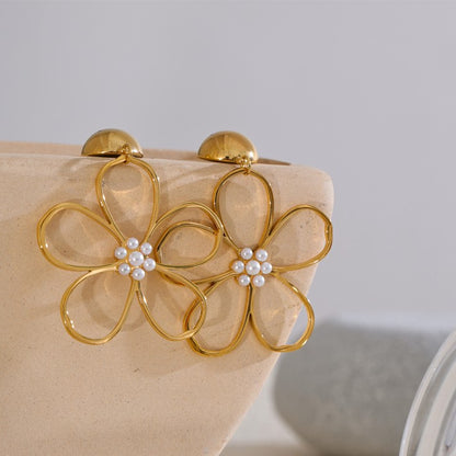 Gold flower-shaped earrings with pearl centers on a beige stand.