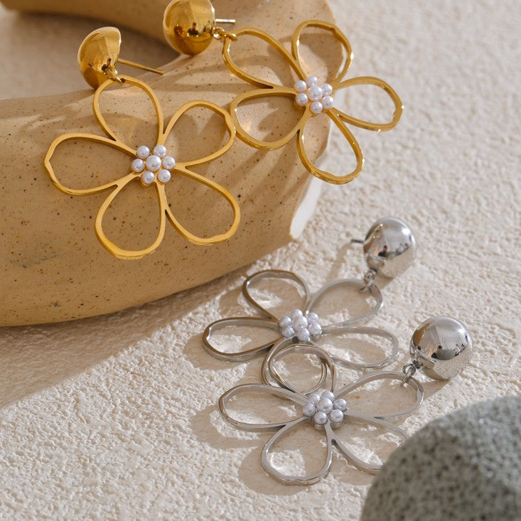 Gold and silver flower-shaped earrings with pearl-like centers on a textured surface.
