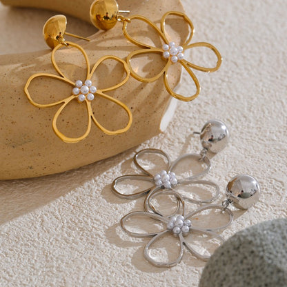 Gold and silver flower-shaped earrings with pearl-like centers on a textured surface.