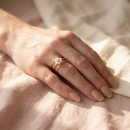 Hand wearing gold rings on a soft fabric background