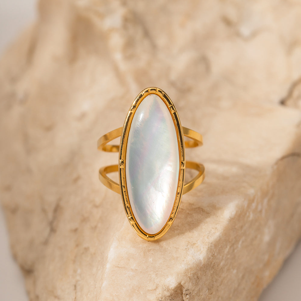 Gold ring with a large, oval, light-colored stone on a textured beige background