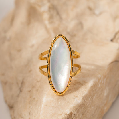 Gold ring with a large, oval, light-colored stone on a textured beige background