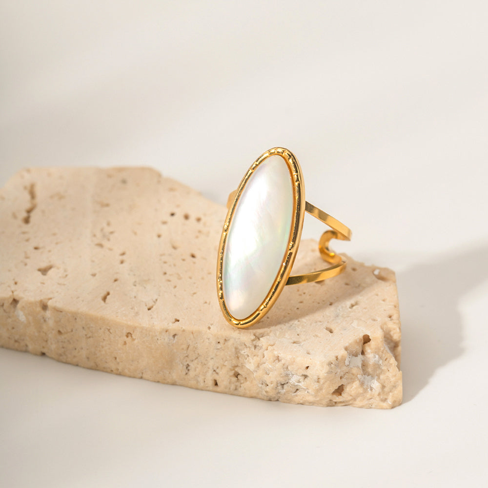 Gold ring with a large white stone on a beige stone surface
