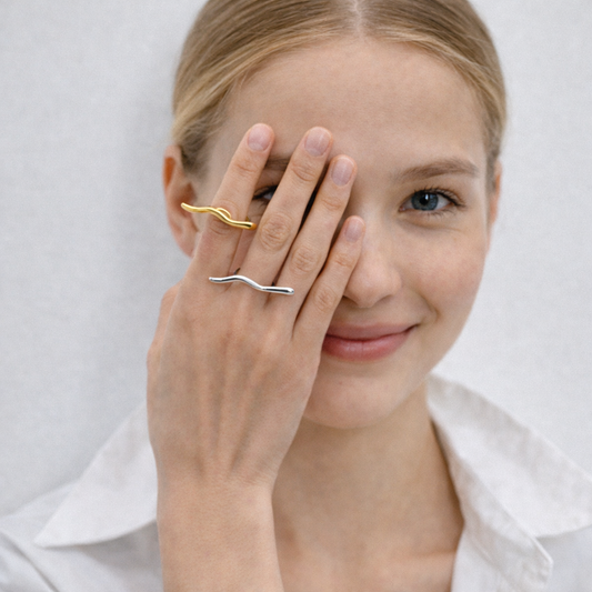 Woman wearing gold and silver rings on a plain background