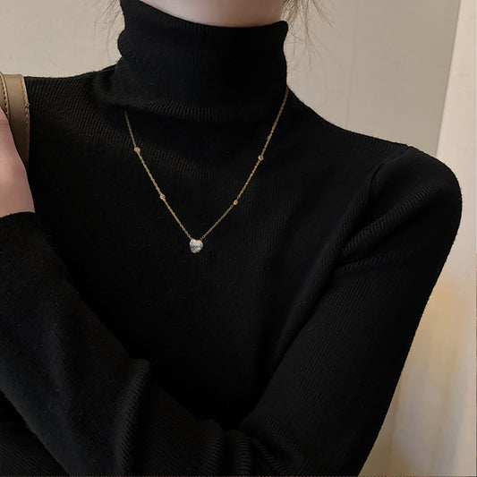 Person wearing a black turtleneck sweater with a gold necklace featuring a heart pendant.
